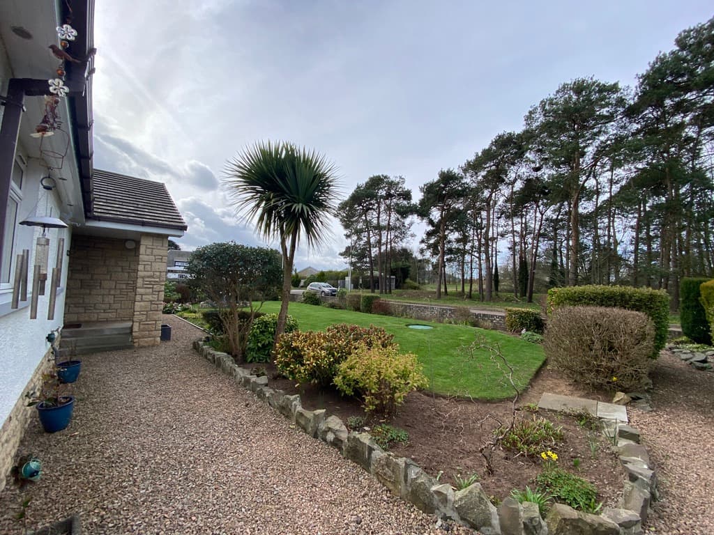 Professionally landscaped garden with manicured lawn, ornamental planting, and countryside views